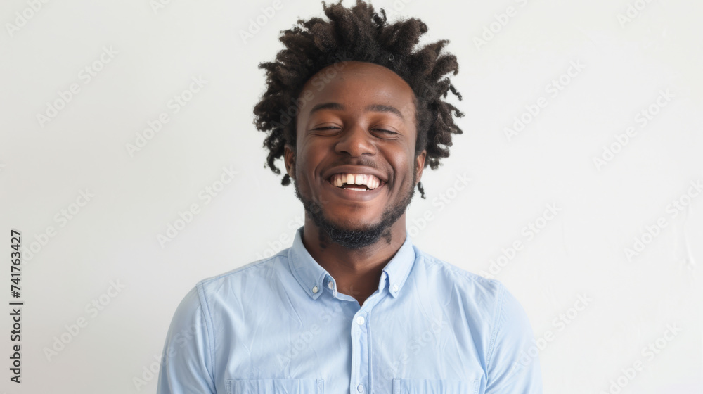 Obraz premium A cheerful man with curly hair smiles widely, wearing a light blue shirt against a white background.