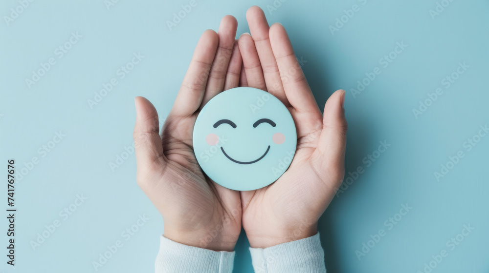 Two hands gently hold a smiling blue sphere against a calming turquoise background, conveying a sense of joy and emotional well-being. - obrazy, fototapety, plakaty 