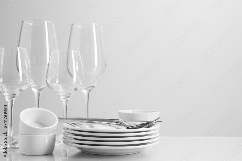 Set of many clean dishware, cutlery and glasses on light table. Space for text Set of many clean dishware, cutlery and glasses on light table. Space for text
