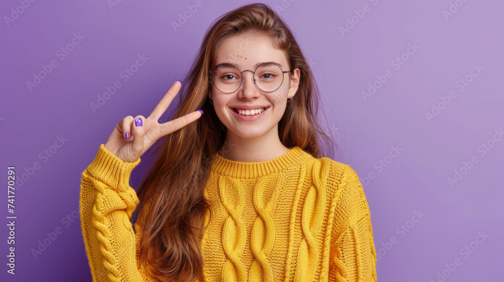 A cheerful young woman in a bright yellow sweater and stylish glasses makes a peace sign with her hand, smiling brightly against a purple background. A cheerful young woman in a bright yellow sweater and stylish glasses makes a peace sign with her hand, smiling brightly against a purple background.