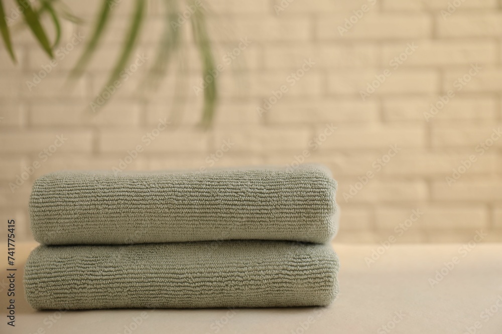 Stacked soft towels and green leaves on white table near brick wall indoors, space for text