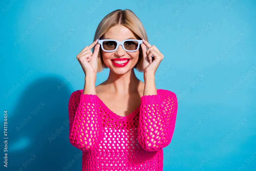 Photo portrait of pretty young girl touch 3d glasses toothy smile dressed stylish pink knitwear outfit isolated on blue color background