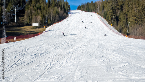 Steep ski slope, chairlift, skiers and snowboarders in Bialka Tatrzanska ski resort in Poland in winter. Wide copy space on the snow below