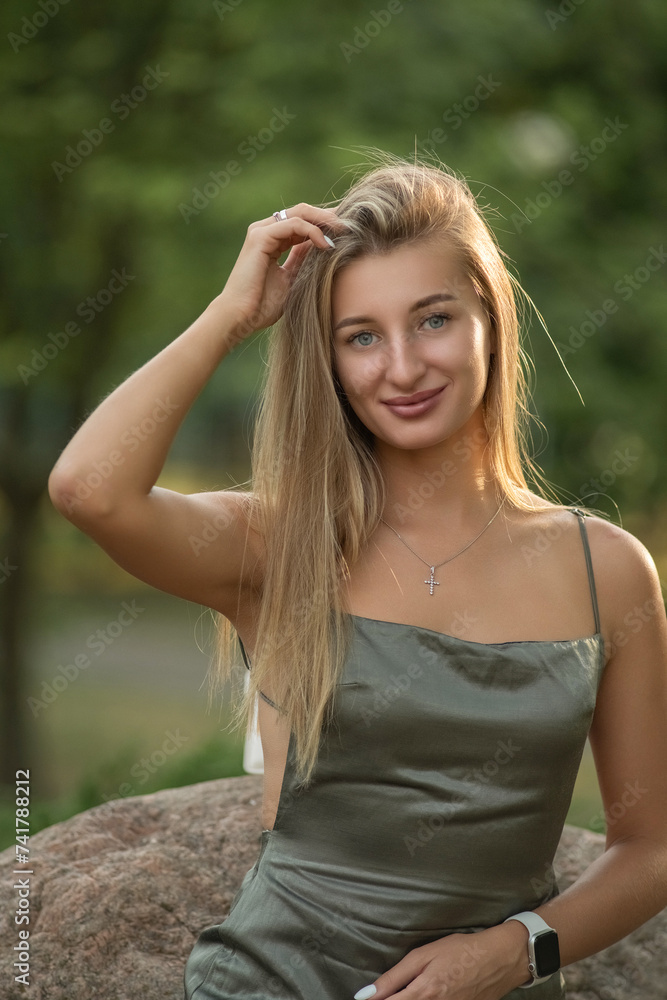 Portrait of a young beautiful blonde girl in a green dress in a city park. Portrait of a young beautiful blonde girl in a green dress in a city park.