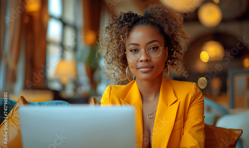 African american woman freelancer in yellow suit sitting in modern cafe or office and working on laptop photo
