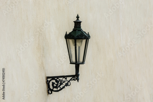 Street lamp on a black iron bracket against a beige wall background.