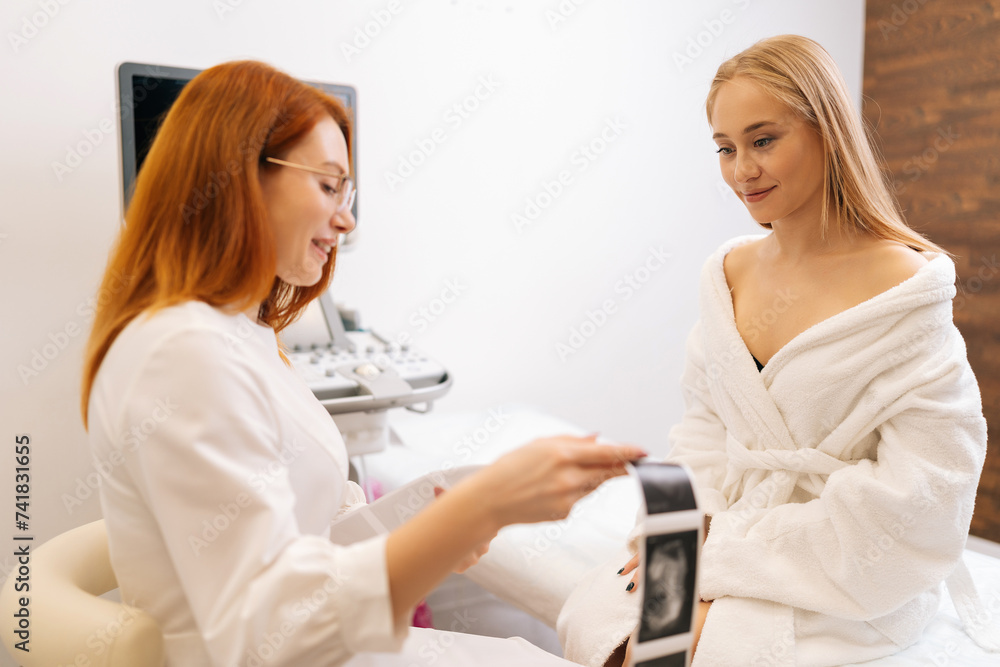 Professional female doctor checking results of ultrasound examination and explaining mage to young woman patient. Doctor explaining results of treatment. Health care and medical women concept. Professional female doctor checking results of ultrasound examination and explaining mage to young woman patient. Doctor explaining results of treatment. Health care and medical women concept.