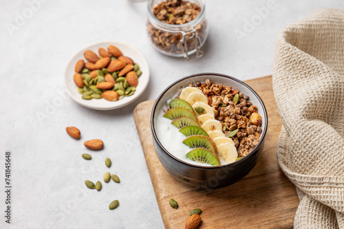 Muesli with yogurt, banana and kiwi in a bowl on a cutting board on a light background.