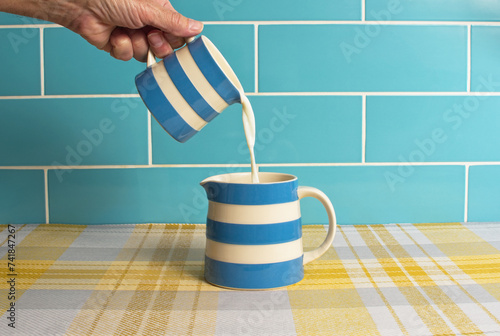 Milk image with a blue and white jug pouring fresh milk into another similar jug. Blue white and yellow colours. Dairy produce concept. photo