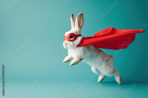 Superhero rabbit, Cute bunny with a red cloak and mask jumping and flying on blue background with copy space. The concept of a superhero, funny pet, leader, funny animal studio shot photo