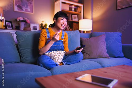 Woman switching channals using remote control while watching TV at home late at night