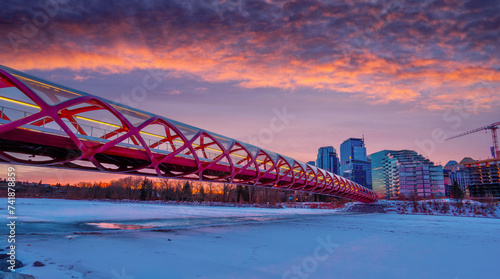 Winter sunrise over the Peace Bridge leading to downtown in Calgary with frozen and snow-covered Bow River.