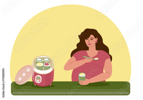 Pregnant young woman eats homemade fruit curd yogurt. A young woman sits at the table and has breakfast, next to an electric yogurt maker. Motherhood, pregnancy, healthy eating, natural vitamins. 