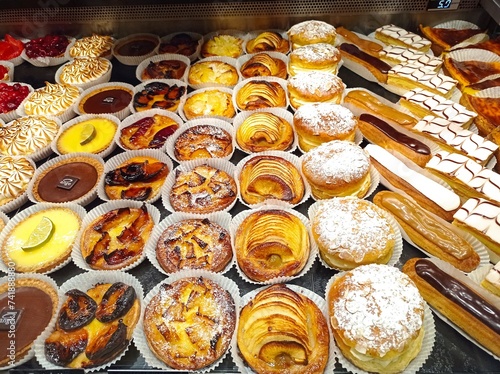 bright french pastries in a baker window, with chou, tropezienne, flan, eclair, and fruits tarts