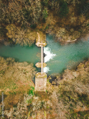 Overhead drone view of a wooden suspension bridge over the crystal-clear river Irati. Winter landscape, leafless trees. Aribe, Navarra, Spain.
