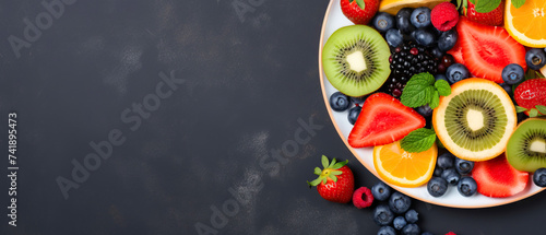Web banner with fresh summer salad of various fruits and berries. Kiwi, orange, strawberry and blueberry on a plate decorated with mint on a table top view, free space for text