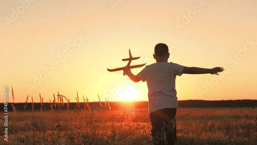 boy runs with plane his hand, child boy plays with toy plane, child son runs happily through field sunset, fantastic dream airplane pilot, cheerful child boy runs happily with toy plane through park