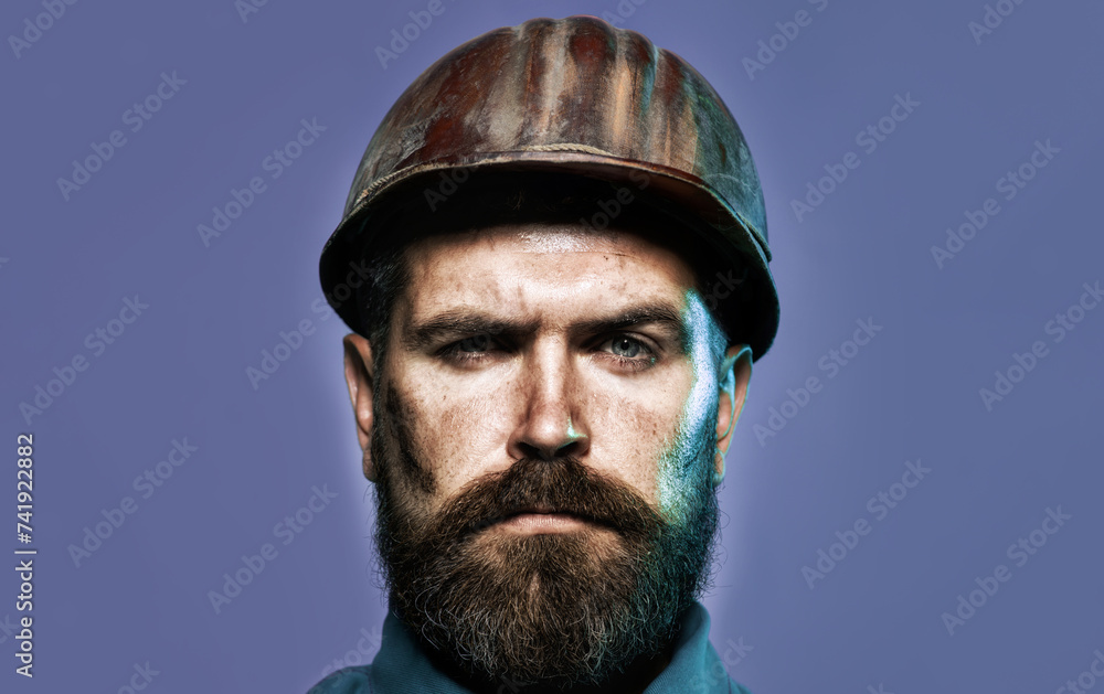 Fototapeta premium Closeup portrait of serious mechanical or industrial worker in safety hardhat. Handsome male builder, contractor, foreman in protective hard hat. Bearded architect or engineer in construction helmet.