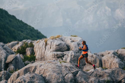 An extreme sportswoman is jogging and running on rocky mountain top.