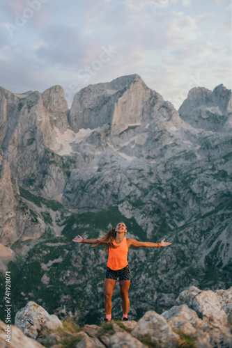 A sportswoman is standing on rocky mountains and experiencing freedom.