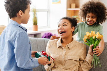 African American family, smiling children giving gift and bouquet of yellow tulips to excited mother