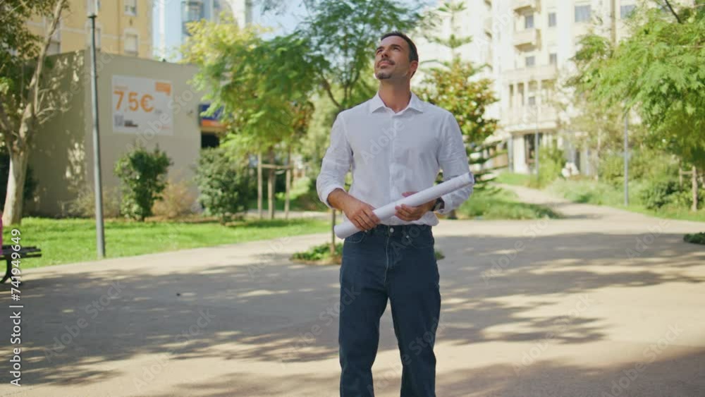 Successful engineer holding project examining houses at summer neighbourhood Successful engineer holding project examining houses at summer neighbourhood