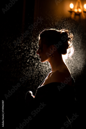 A beautiful female profile in contour lighting. A girl with her hair pulled back against a dark background.