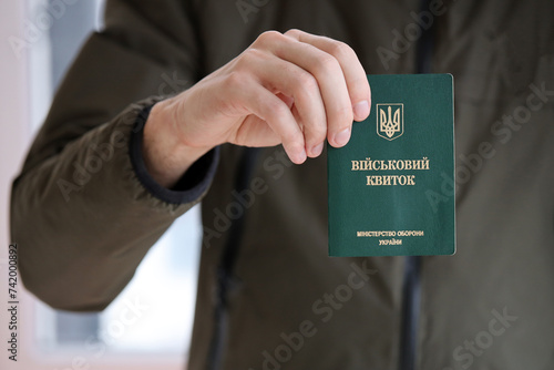 Young ukrainian conscript soldier shows his military token or army ID ticket indoors close up photo