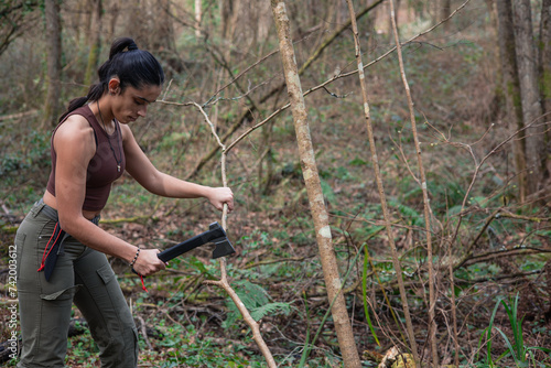 Фотография adventurous survival girl cutting branches with an axe in the forest