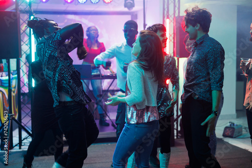 Friends dancing at concert in nightclub, having fun and moving on dancefloor. People partying and enjoying dj live music performance on stage while attending discotheque in club