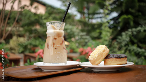 Iced coffee with chocolate and chesee donuts on the wooden table against foliage background. Refreshing coffee drink business lunch. photo