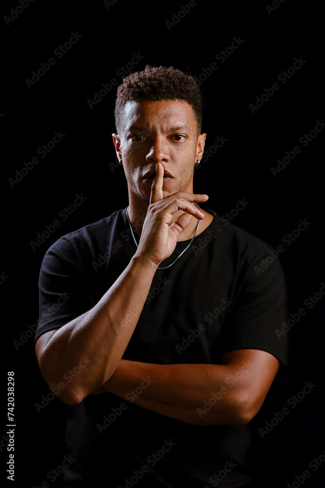 Low key portrait of young African man making silence gesture