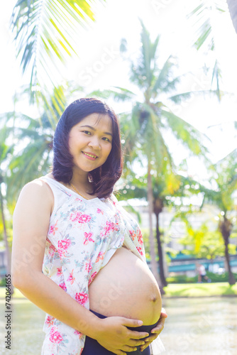 Asian young happy pregnant woman relaxing and enjoying life in nature park sunshine ligfht photo