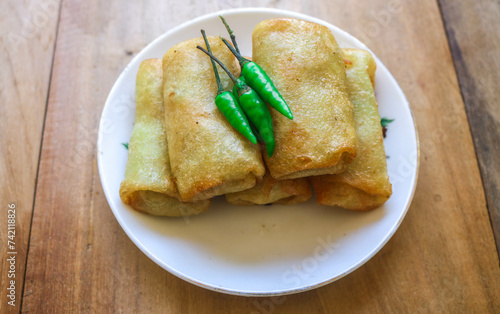 Lumpia or fried spring rolls are a food made from flour filled with vegetables such as carrots, cabbage, sprouts and eggs. Lumpia or fried spring rolls on a white plate served with chili photo