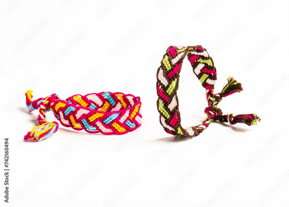 Fototapeta premium Multicolored woven DIY friendship bracelets handmade of embroidery bright thread with knots isolated on white background