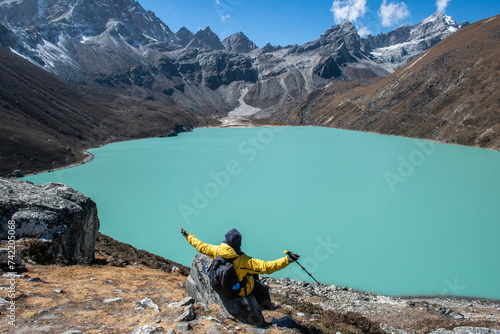 Trekker sitting on the rock and looking to the beautiful view of Gokyo lakes the sacred green lake in Gokyo village one of the most tourist attraction place in Solukhumbu district of Nepal. photo