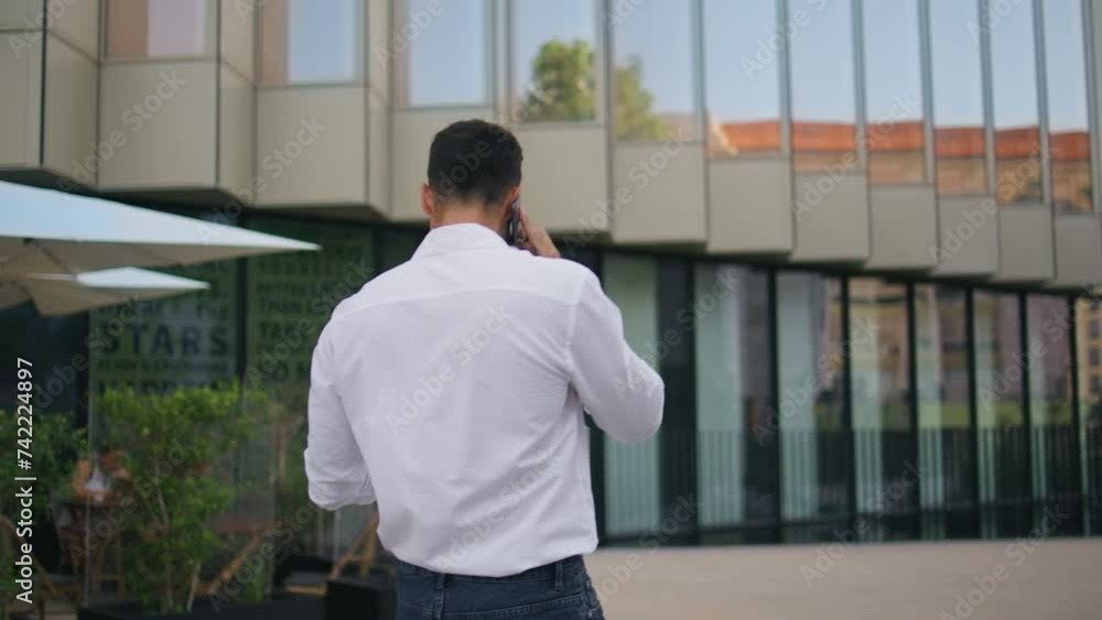 Successful entrepreneur making call walking in modern city back view. Man going
