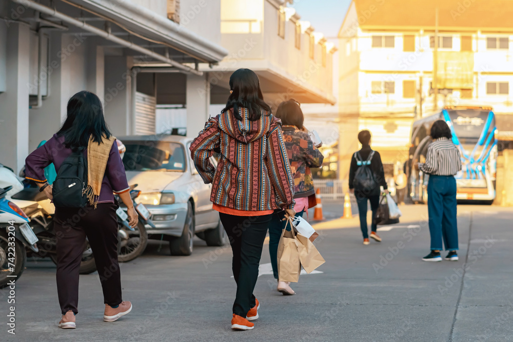 Back view of Asian elderly woman traveler in casual clothes walks down a street with travel bag in morning. Senior woman tourist walks with her travel bag. Vacation and travel elderly people concept. Back view of Asian elderly woman traveler in casual clothes walks down a street with travel bag in morning. Senior woman tourist walks with her travel bag. Vacation and travel elderly people concept.