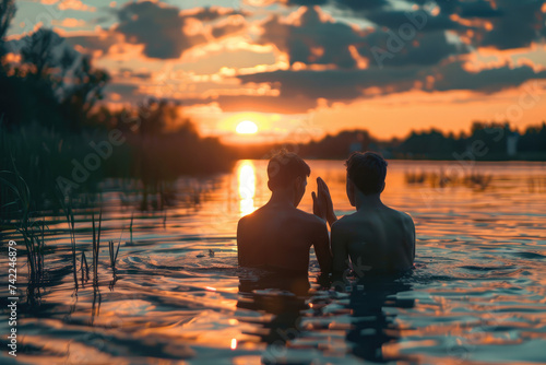 Baptism. Portrait of two young man praying in the water at sunset © Kien