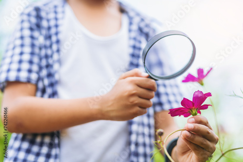 Boy with magnifying glass explorer and learning the nature, flower garden backyard. Selected focus