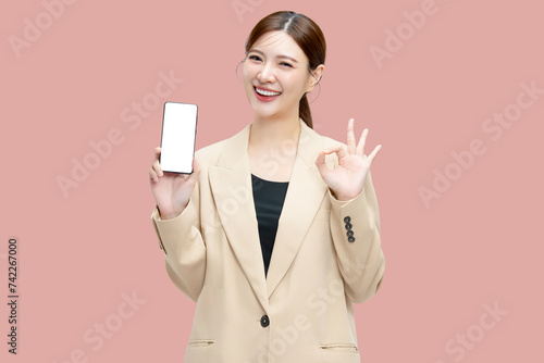 Beautiful Asian business woman showing smartphone mockup of blank screen with ok hand signal on pink background. photo