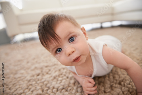 Sweet, cute and portrait of baby on carpet playing for child development in living room at home. Happy, adorable and young infant, toddler or kid learning to crawl on floor rug in modern house.