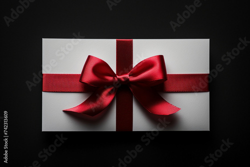 Blank white gift card, red ribbon bow, black background, shadow – minimal, conceptual elegance in a simple, sophisticated presentation.