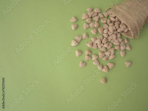 Extruded bran in the shape of a heart is poured out of a cloth bag onto a green background with space for text