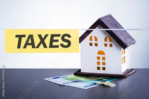 The concept of paying state property tax in Europe.  Model house on pile euro money banknotes and text TAXES. photo