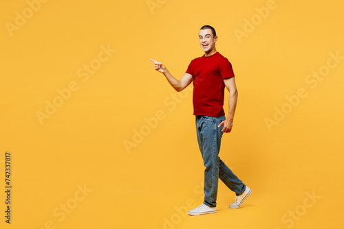 Full body side profile view smiling happy cheerful young middle eastern man he wear red t-shirt casual clothes walk go point aside isolated on plain yellow orange background studio. Lifestyle concept