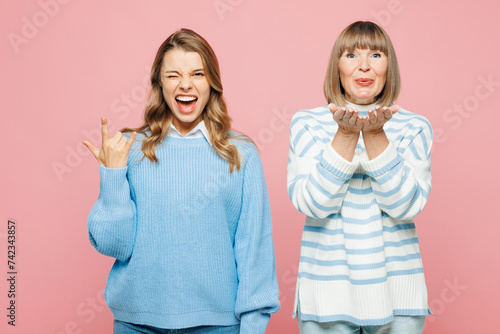 Elder parent mom 50s year old with young adult daughter two women together wear blue casual clothes do horns up gesture blow air kiss isolated on plain pastel light pink background Family day concept photo