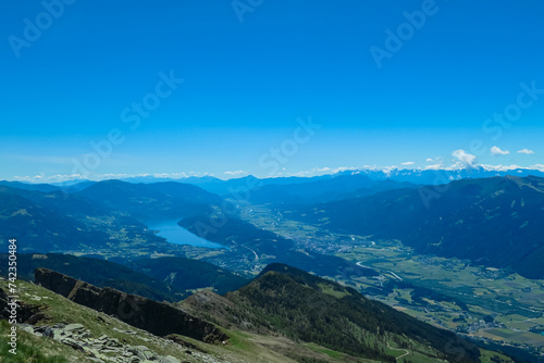 Idyllic hiking trail on alpine meadow with scenic view of lake Millstatt seen from mountain peak Boese Nase in Ankogel Group, Carinthia, Austria. Remote landscape in majestic Austrian Alps in summer