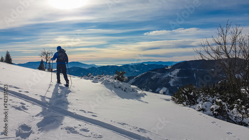 Man with snowshoes in snow covered meadow on way to Hochanger, Muerzsteg Alps, Styria, Austria. Panoramic view of snow capped mountain peaks Hochschwab massif. Winter wonderland remote Austrian Alps