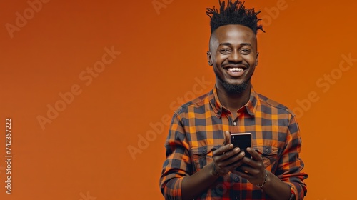 African American boy looking at cell phone, smiling, flat orange background, there is space on the left to write, space for copy